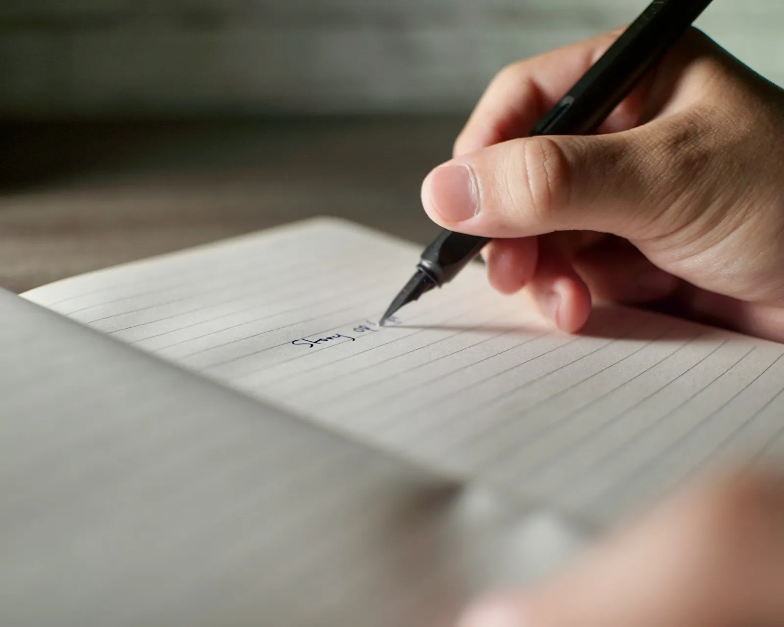 A hand writing in a notebook with a pen